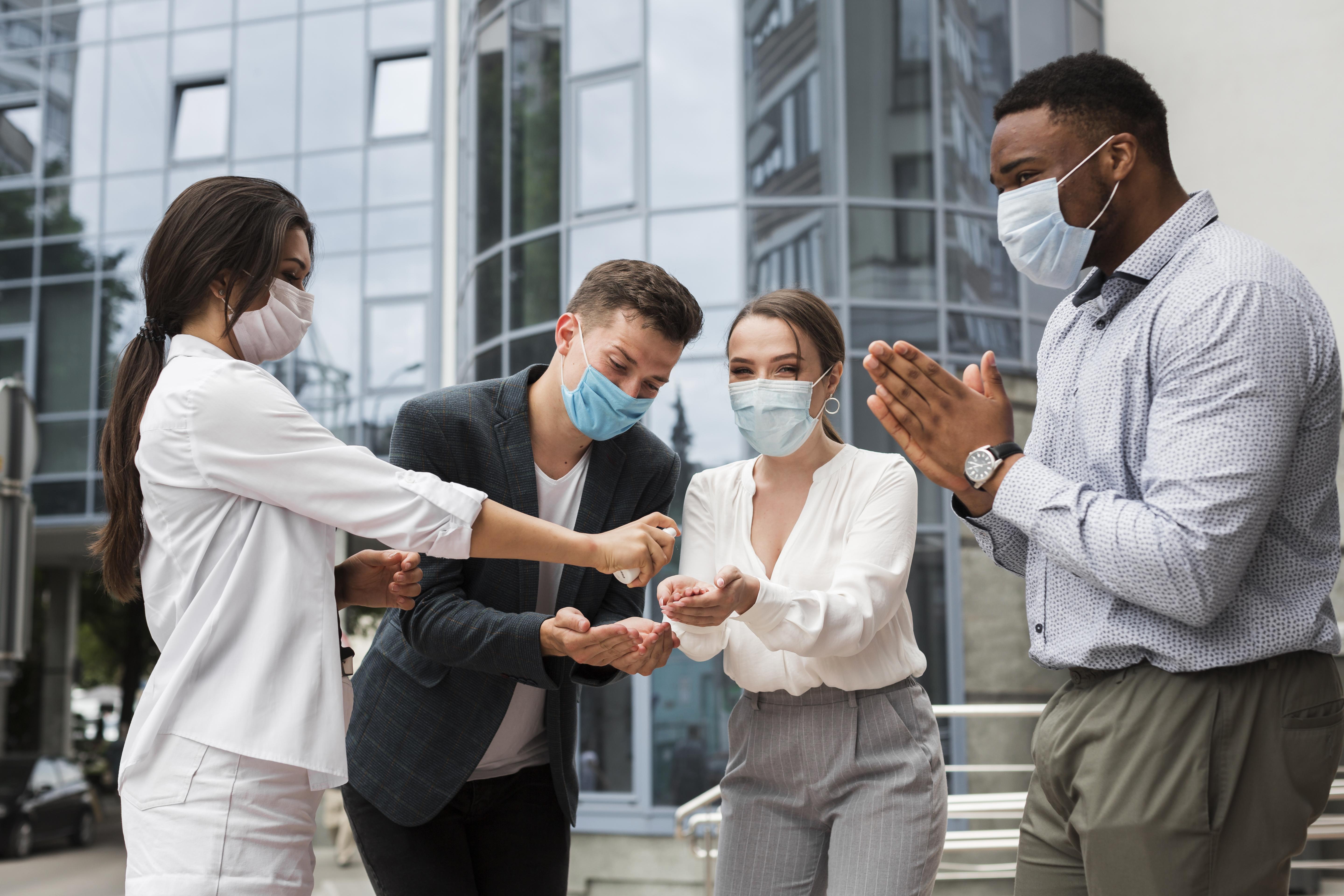 coworkers disinfecting hands outdoors pandemic while wearing masks